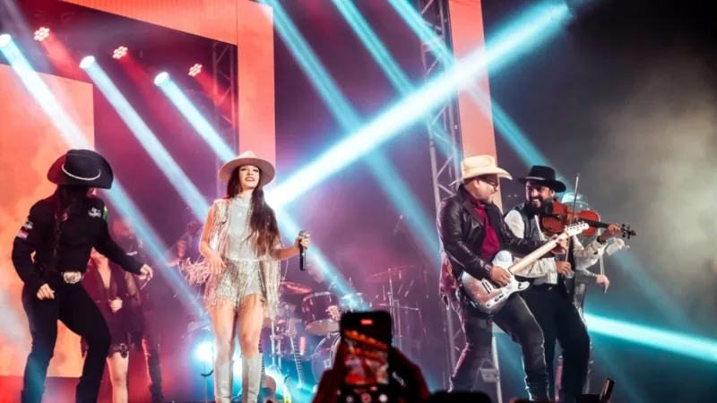 A banda Dallas Country se apresenta com energia em um show em Aracruz, com iluminação vibrante e público animado.
