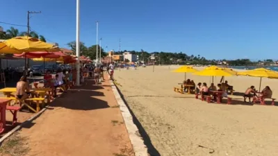 Praia de Meaípe, em Guarapari, com guarda-sóis amarelos e turistas em um dia de sol