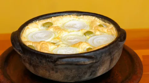 Torta capixaba coberta com ovos e rodelas de cebola na panela de barro, prato da mesma família da frigideira de siri