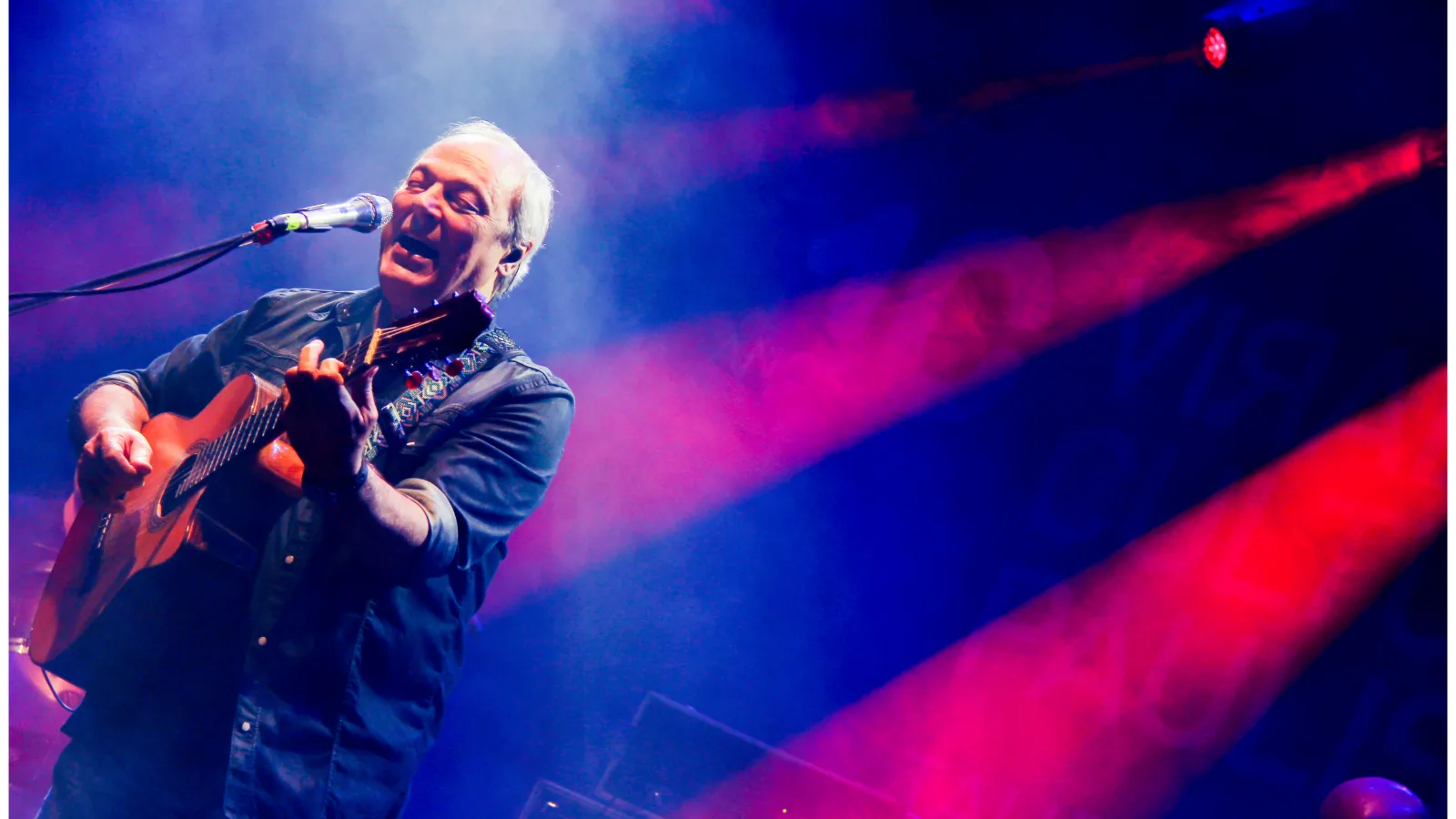 Toquinho toca violão no palco sob luzes coloridas
